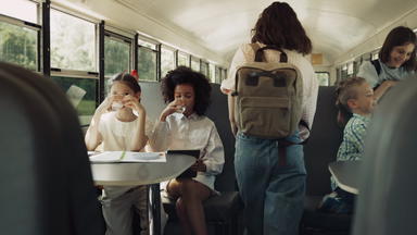 多元文化的学生坐着学校公共汽车早....学生登上校车
